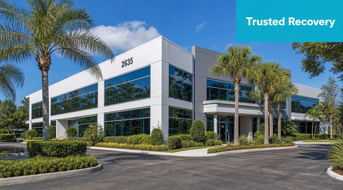 A professional modern commercial office building surrounded by lush green landscaping under a bright blue sky.